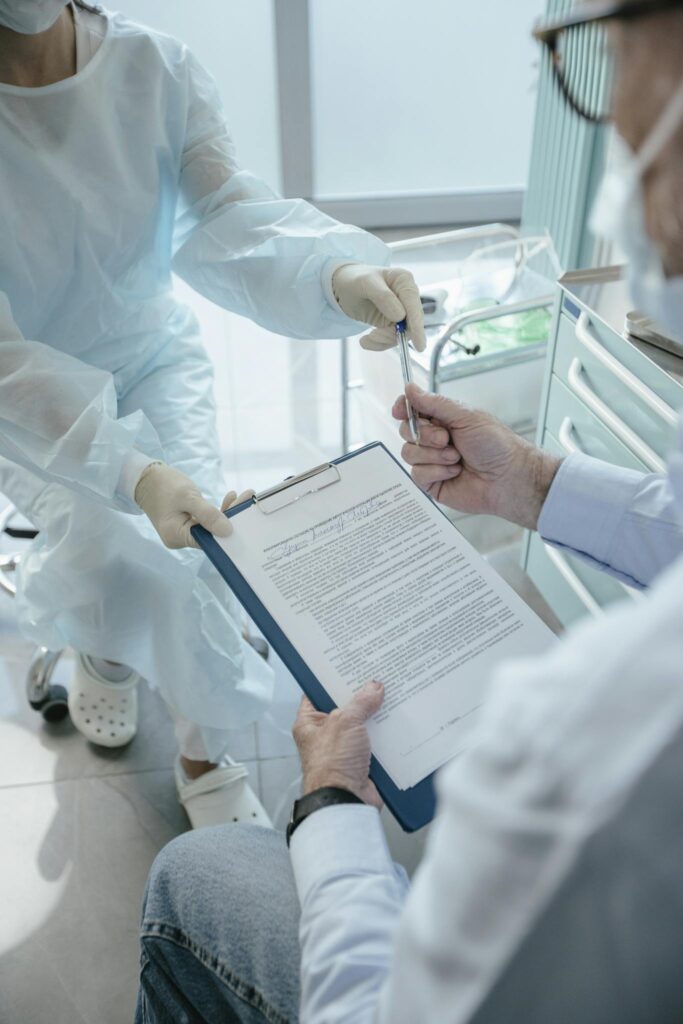 A patient in a medical office receives a document to sign from a healthcare professional for processing.